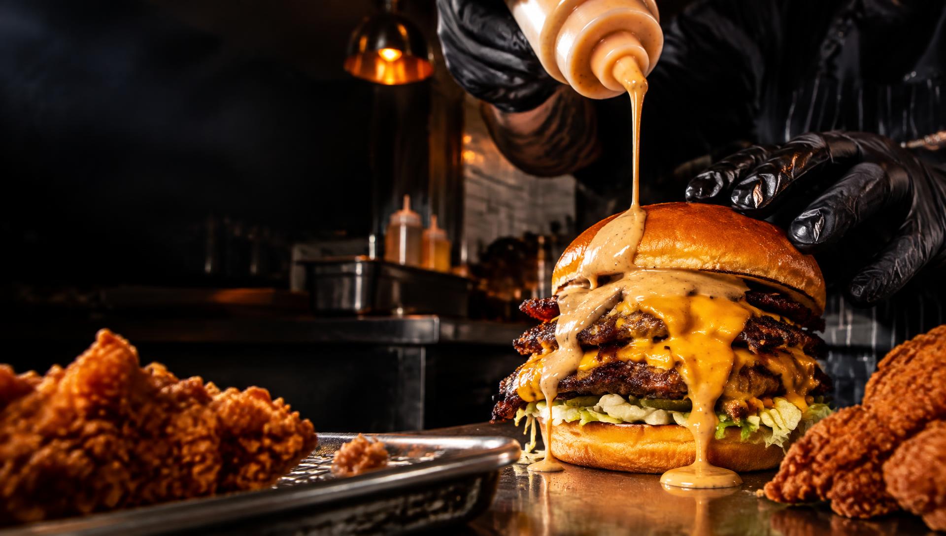 Sauce being poured over a freshly made burger